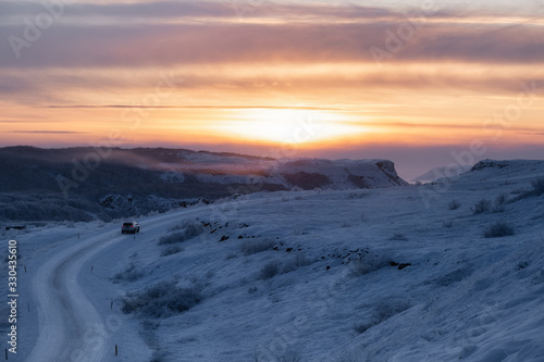 winter sunset in the mountains with snow, road and a car driving
