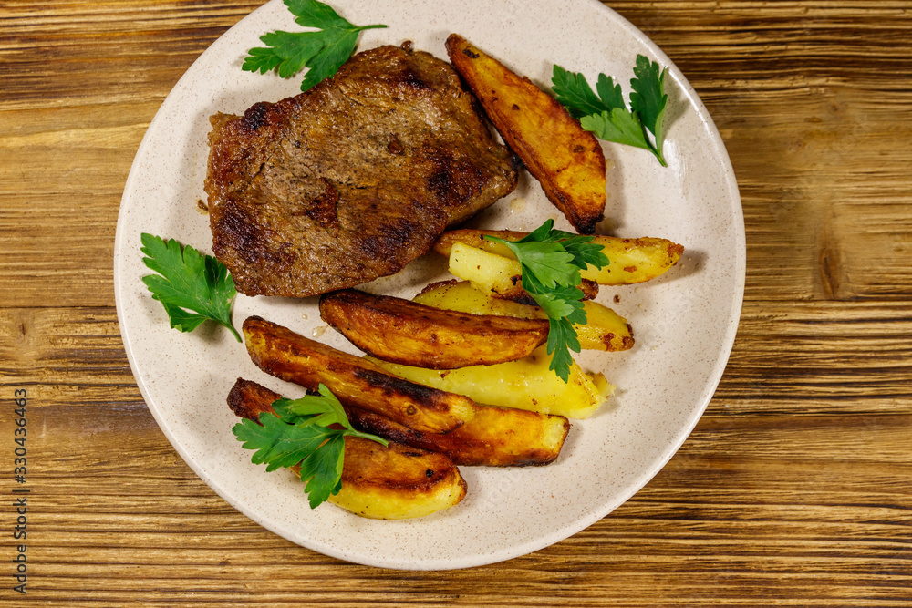 Fried beef steak with potato wedges on wooden table. Top view Fried beef steak with potato wedges on wooden table. Top view