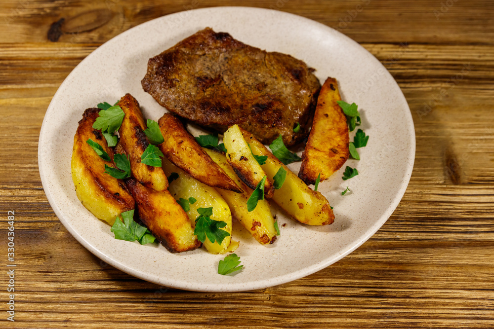 Fried beef steak with potato wedges on wooden table Fried beef steak with potato wedges on wooden table