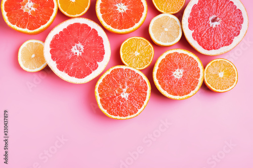 Flat lay composition with halves of different citrus fruits on pink background.