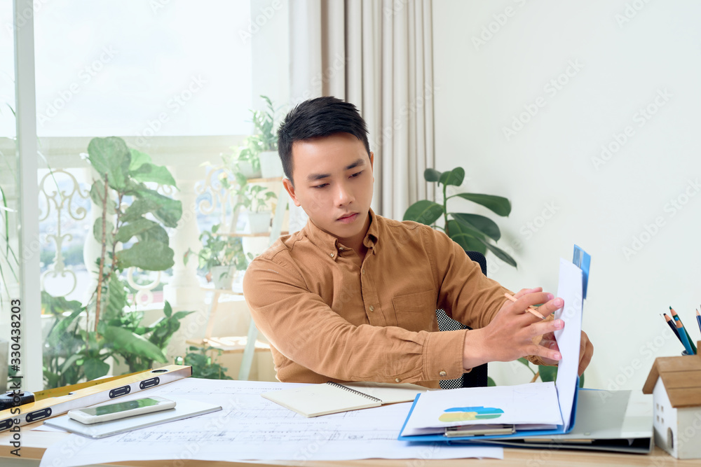 Male architect working with blueprint at his office
