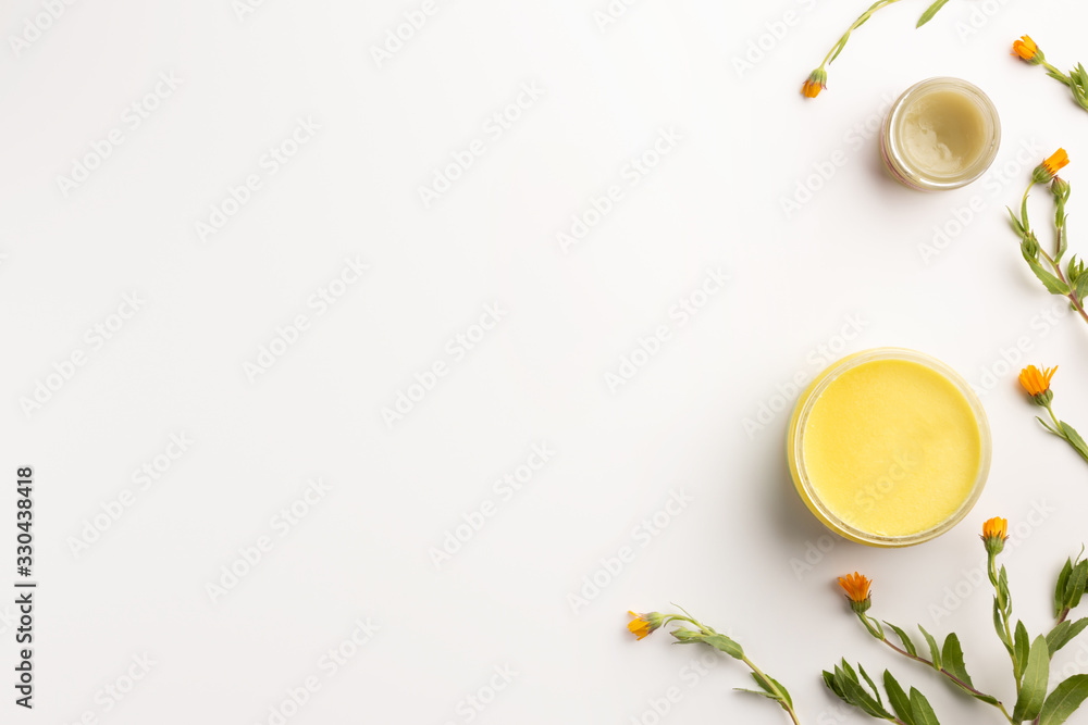 Organic cosmetic concept. Flowers of calendula and jar of skin care cream, isolated on white background. Flat lay, top view, copy space.