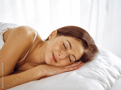 Beautiful young brunette woman sleeping while lying in bed comfortably and blissfully. Good morning concept