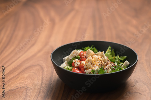 Healthy light salad with cherry tomatoes, mozzarella and frisee in black bowl on walnut surface