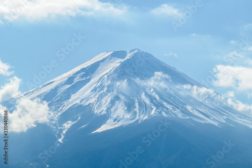 A close up view on Mt Fuji from the side of Kawaguchiko Lake, Japan. The mountain is hiding behind the clouds. Top of the volcano covered with a snow layer. Serenity and calmness. Calm lake's surface