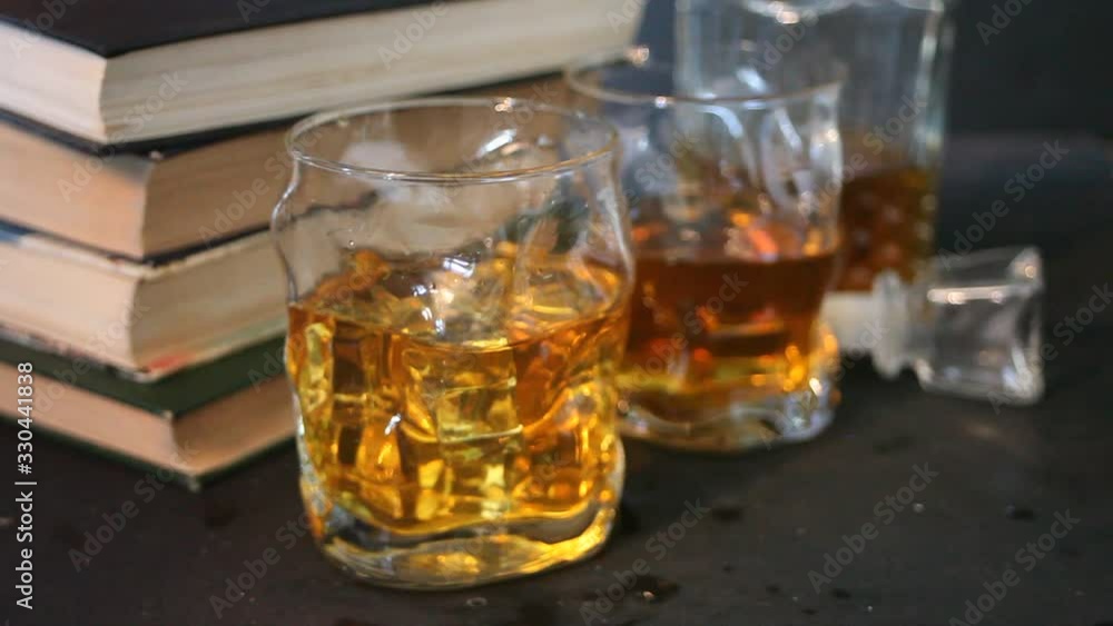 whiskey with ice on a wooden table. Nearby hands put a old books whiskey with ice on a wooden table. Nearby hands put a old books