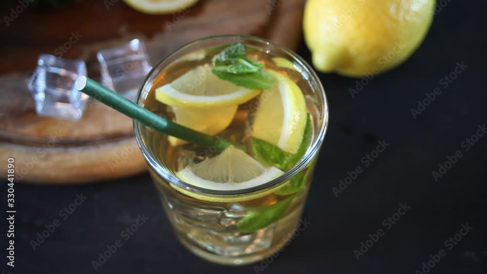 Glass of cold refreshment tea with ice and lemon fruit. Woman hand put a paper straw in the glass Glass of cold refreshment tea with ice and lemon fruit. Woman hand put a paper straw in the glass
