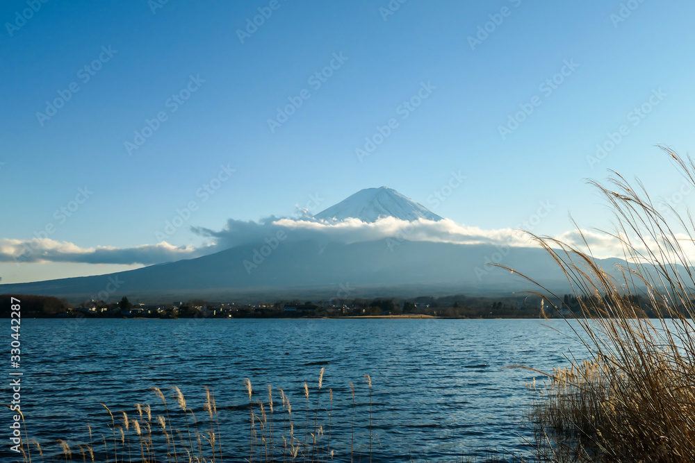 A close up view on Mt Fuji from the side of Kawaguchiko Lake, Japan. The mountain is hiding behind the clouds. Top of the volcano covered with a snow layer. Serenity and calmness. Calm lake's surface