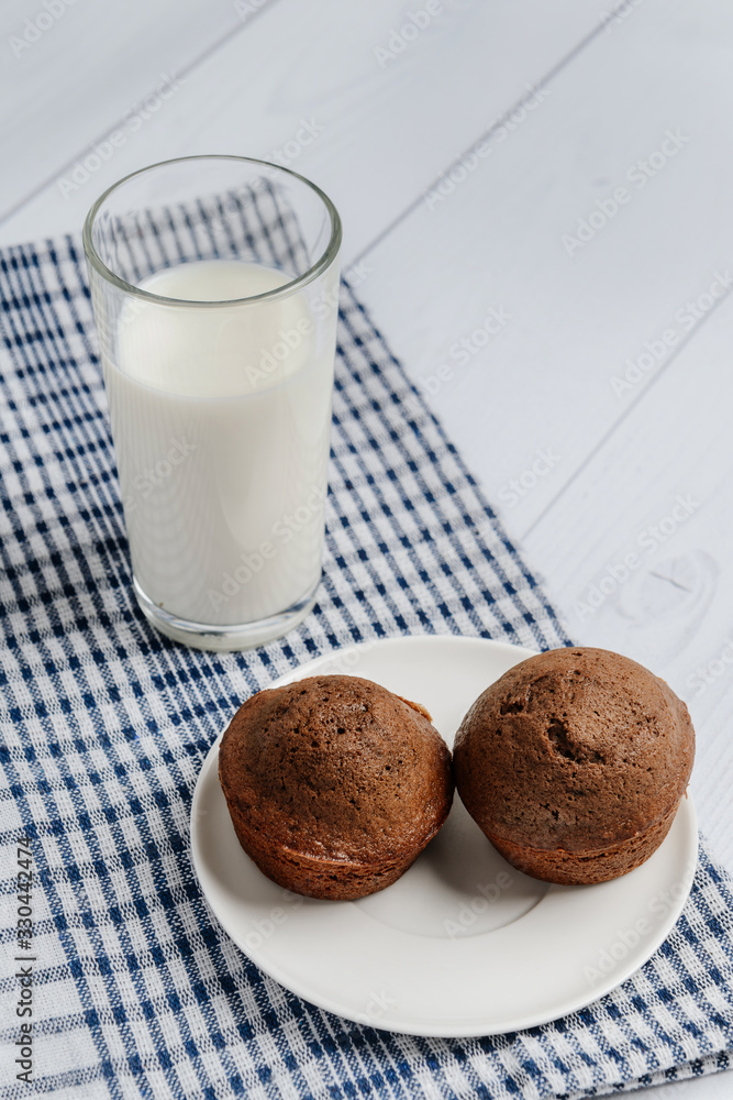 a glass of milk on a napkin and two muffins on a dish. Breakfast concept. a glass of milk on a napkin and two muffins on a dish. Breakfast concept.