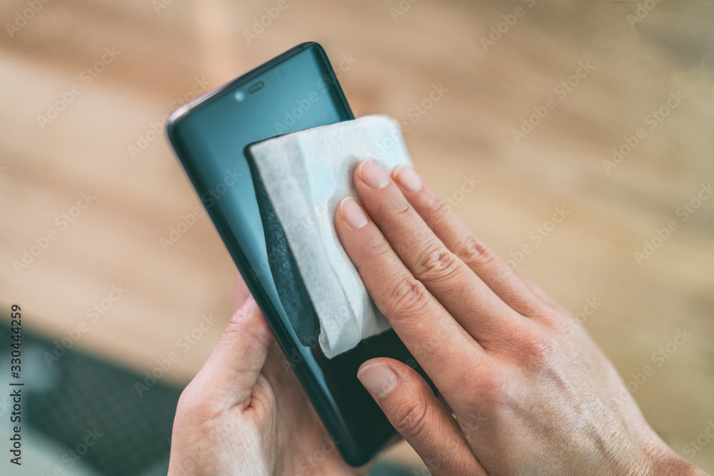 Cleaning mobile phone screen with disinfecting wet wipes for clean smartphone preventive wiping for COVID-19 Coronavirus outbreak contamination prevention. - obrazy, fototapety, plakaty 