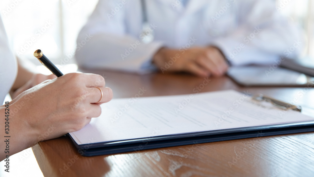 Close up young woman holding pen, ready to sign medical insurance contract with family doctor. Female patient putting signature on agreement with physician during meeting in clinic hospital. Close up young woman holding pen, ready to sign medical insurance contract with family doctor. Female patient putting signature on agreement with physician during meeting in clinic hospital.