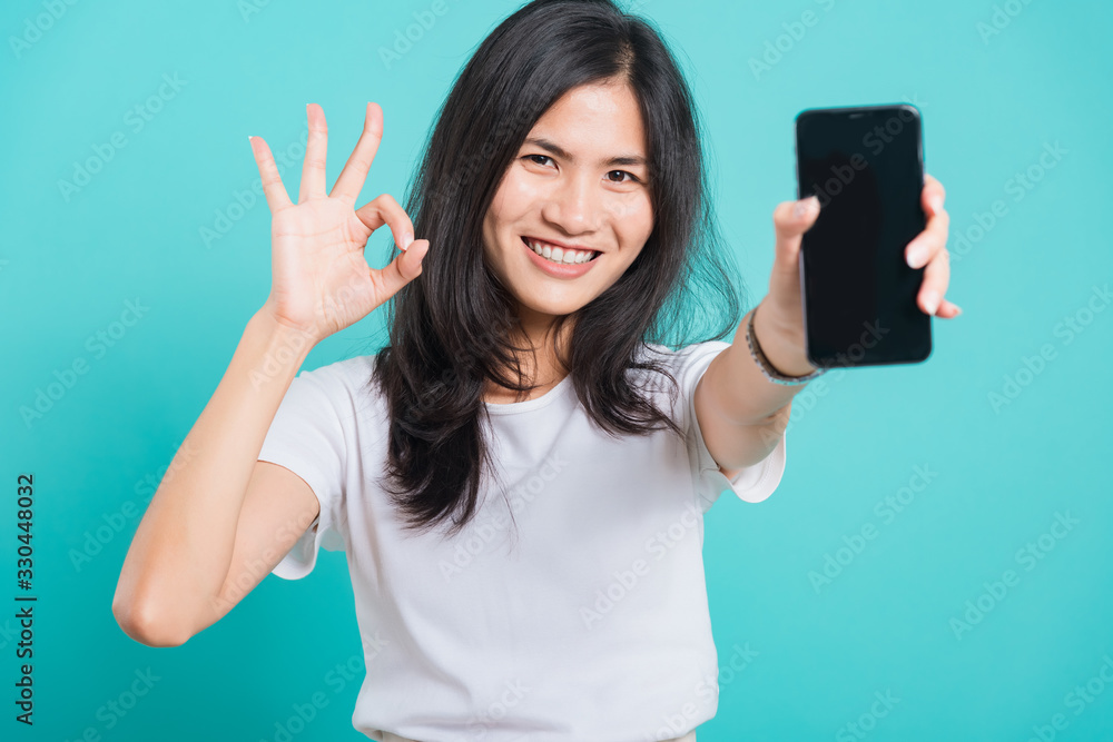 young woman standing smile, holding mobile phone and showing ok gesture young woman standing smile, holding mobile phone and showing ok gesture