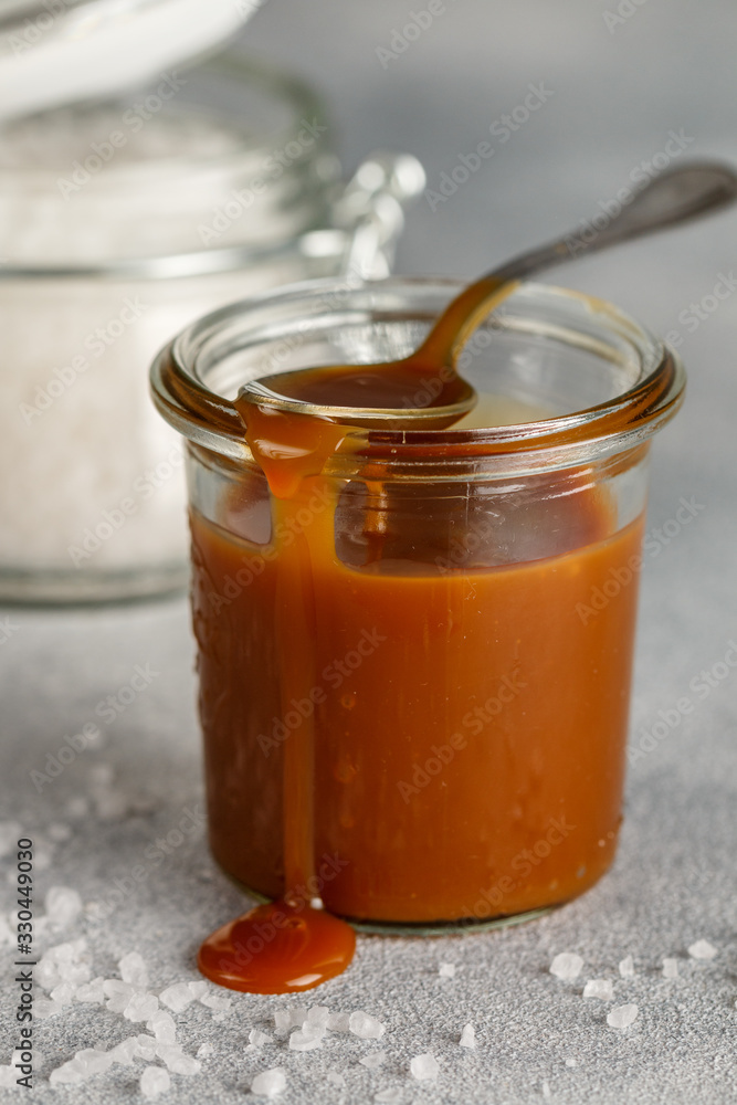 Homemade salted caramel in a glass jar. Delicious sauce with sea salt for ice cream and desserts. Selective focus Homemade salted caramel in a glass jar. Delicious sauce with sea salt for ice cream and desserts. Selective focus