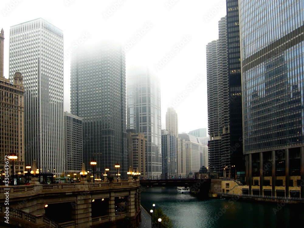 Downtown Chicago in the autumn under fog with Chicago River, skyscrapers, glass office towers and bridge. the green canal and yellow street lights.