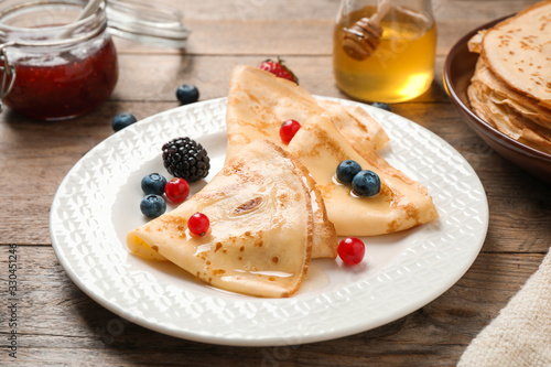 Delicious thin pancakes with berries on wooden table