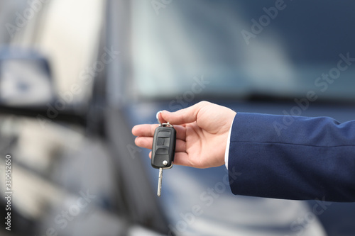 Man holding key in modern auto dealership, closeup. Buying new car