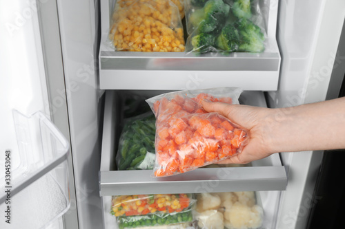 Woman taking plastic bag with frozen carrot from refrigerator, closeup