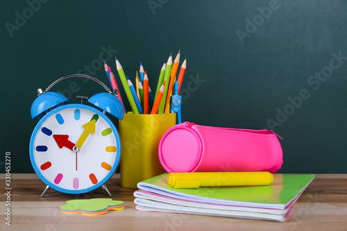 Composition with stationery and alarm clock on table near chalkboard. Doing homework photo