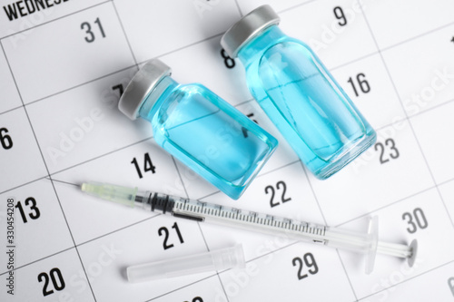Vial and syringe on calendar, flat lay. Vaccination and immunization