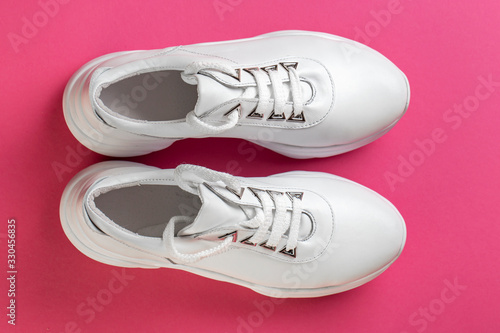 Pair of fashion shoes on colorful background. New white sneakers on pink background, copy space.