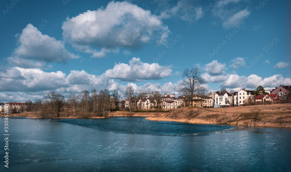 Eco-friendly cottage village on the shore of the lake. Bright spring landscape with houses near a frozen lake.