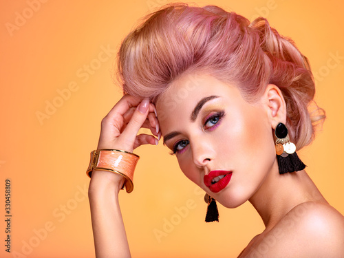 Beautiful woman with creative hairstyle, vivid makeup. Fashionable girl. Beautiful face of young woman with red lips. Stunning blonde girl. Bright eye makeup. Attractive caucasian model with earrings photo