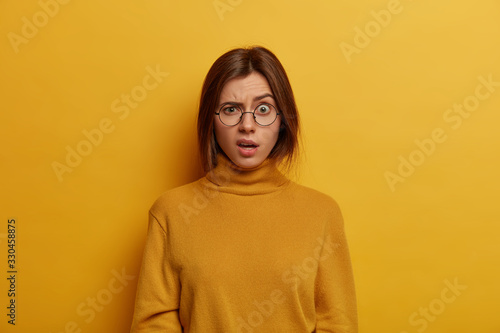 Fotografie Indignant puzzled young woman raises eyebrows and looks with shocked expression
