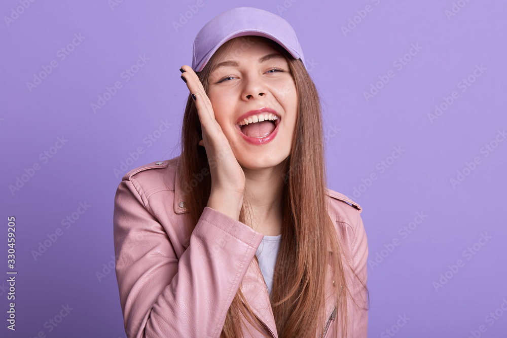 Close up portrait of cheerful sincere magnetic posing isolated over lilac background in studio, opening mouth widely, putting one hand on cheeck, laughing, having fun, feeling good. Emotions concept. Close up portrait of cheerful sincere magnetic posing isolated over lilac background in studio, opening mouth widely, putting one hand on cheeck, laughing, having fun, feeling good. Emotions concept.