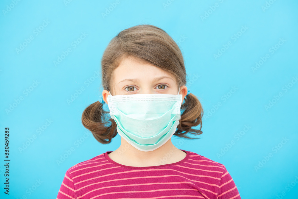 Little girl in a protective medical face mask on a blue background. Coronavirus Protection Concept, COVID-19.