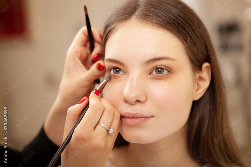 Young beautiful woman with flawless skin getting her makeup done by professional makeup artist Young beautiful woman with flawless skin getting her makeup done by professional makeup artist