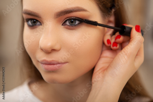 Close up of a gorgeous woman smiling while professional makeup artist applying mascara on her lashes