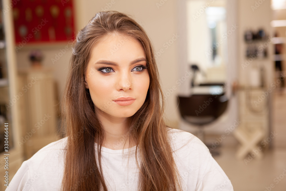 Attractive young woman with professional makeup looking away dreamily, sitting at beauty salon