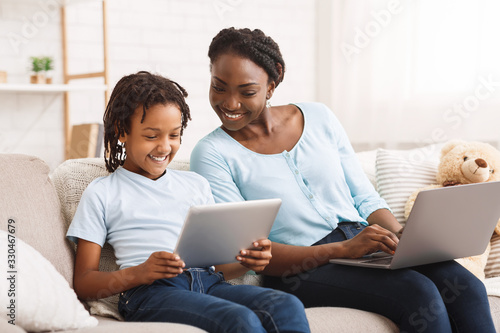 Afro mom and daughter doing school homework on sofa