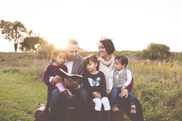 Beautiful cheerful family with a mother, father and three kids reading the Bible in the park