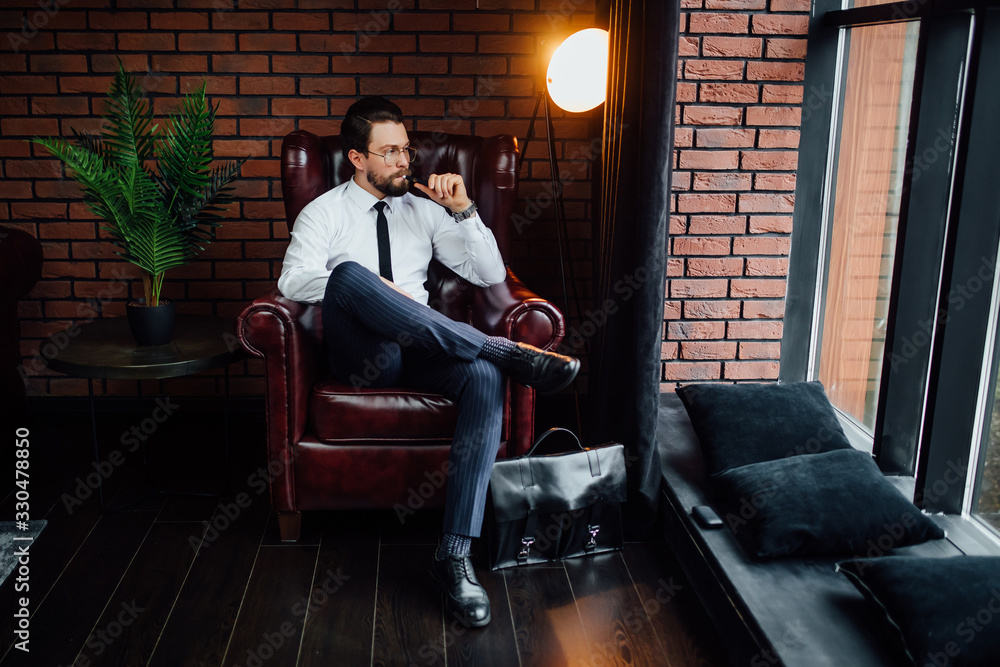 Obraz premium Millionaire man resting and relaxing while sitting on sofa in luxury room. Handsome man smoking cigar.