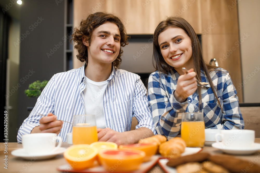 Portrait of pretty couple in love eating breakfast together in morning at kitchen, happy family, romantic, healthy food, cornflakes with milk, orange and croissant at the table