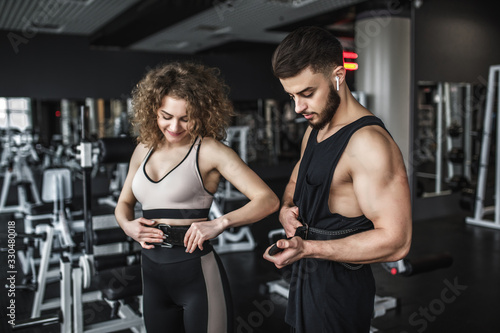 Slim woman wearing sport wears with belt, and her personal trainer during training in gym