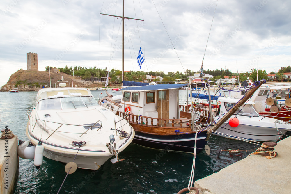 Fototapeta premium Greece. Yachts and boats at the pier on the background of the ancient fortress in Nea fokea. Cassandra. Chalkidiki. Pleasure and fishing boats in the Harbor. An ancient fortress on the coast.