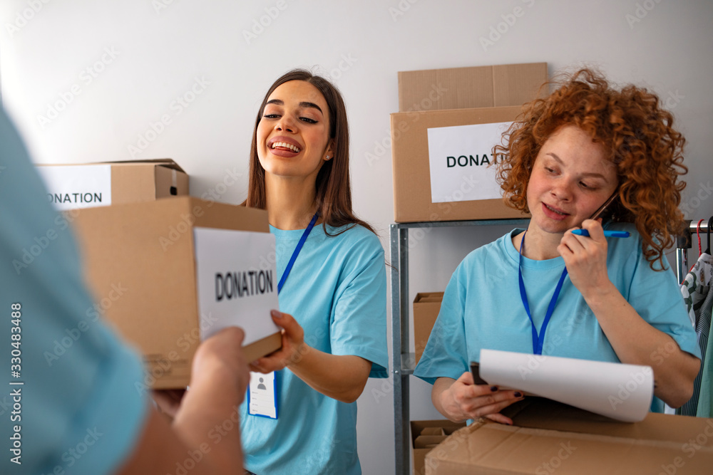 Male and female volunteers sort donations during food drive. Male and female teenage food bank volunteers sort canned food items in cardboard boxes. Small mixed race group of people Male and female volunteers sort donations during food drive. Male and female teenage food bank volunteers sort canned food items in cardboard boxes. Small mixed race group of people