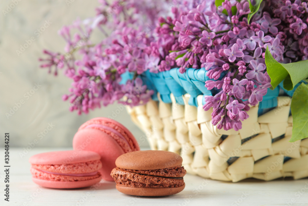 Spring flowers. Twigs of blooming lilac in a wicker basket and macaroon cake on a light concrete background Spring flowers. Twigs of blooming lilac in a wicker basket and macaroon cake on a light concrete background