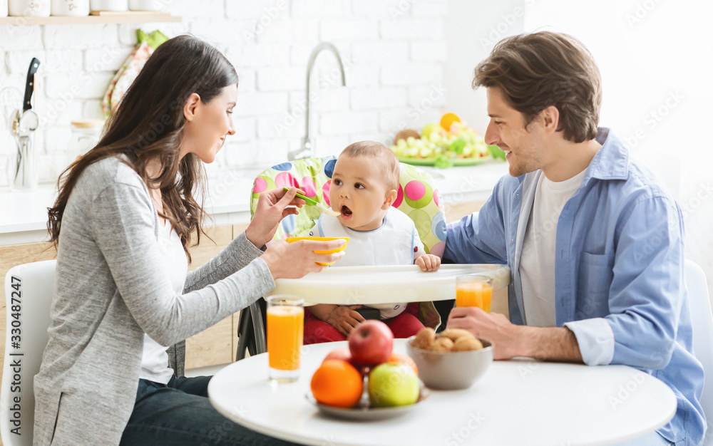 Happy parents feeding baby son at home kitchen Happy parents feeding baby son at home kitchen