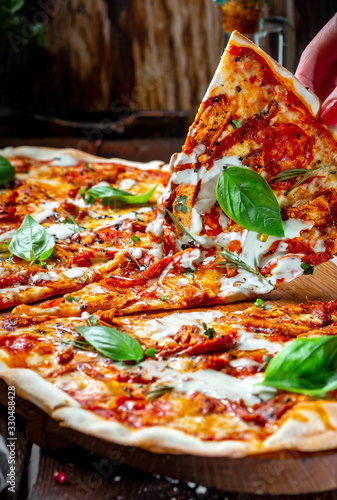 Hand takes a piece of Long pizza Margarita with sun-dried tomatoes and Basil on a wooden Board. Italian cuisine rustic style