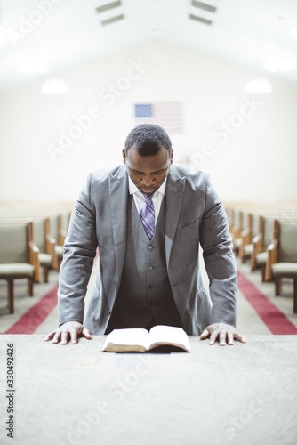 фотографія African-American male praying with his head down looking at the Bible at the chu