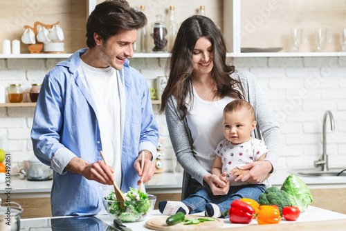 Parents with baby cooking organic healthy lunch at kitchen