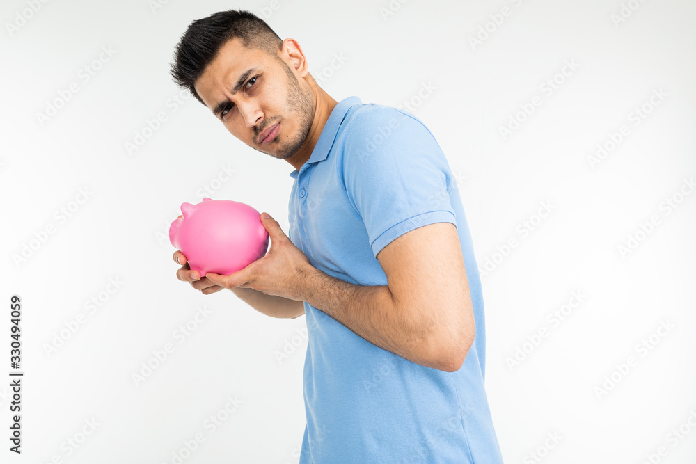 young man in a blue tank holds a piggy bank and refuses on a white studio background young man in a blue tank holds a piggy bank and refuses on a white studio background