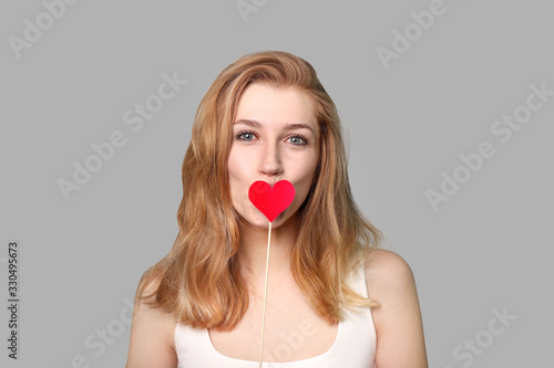 Portrait of beautiful young woman with heart on grey background © LumenSt