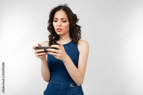serious girl in a blue dress with a smartphone in his hand on a gray studio background