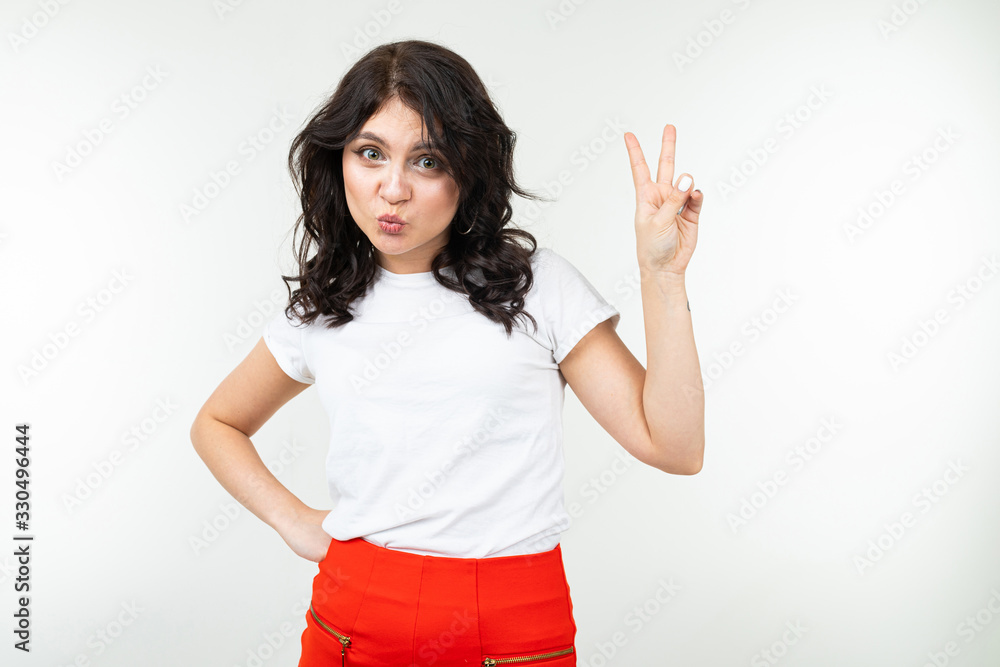joyful girl in a white T-shirt shows two fingers on a white background joyful girl in a white T-shirt shows two fingers on a white background