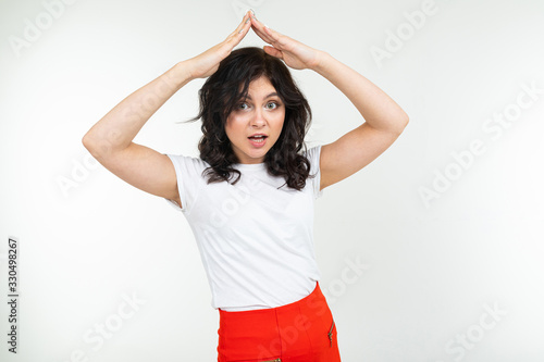 girl shows a safety sign while holding her hands over her head in the form of a roof on a white studio background © Ivan Traimak