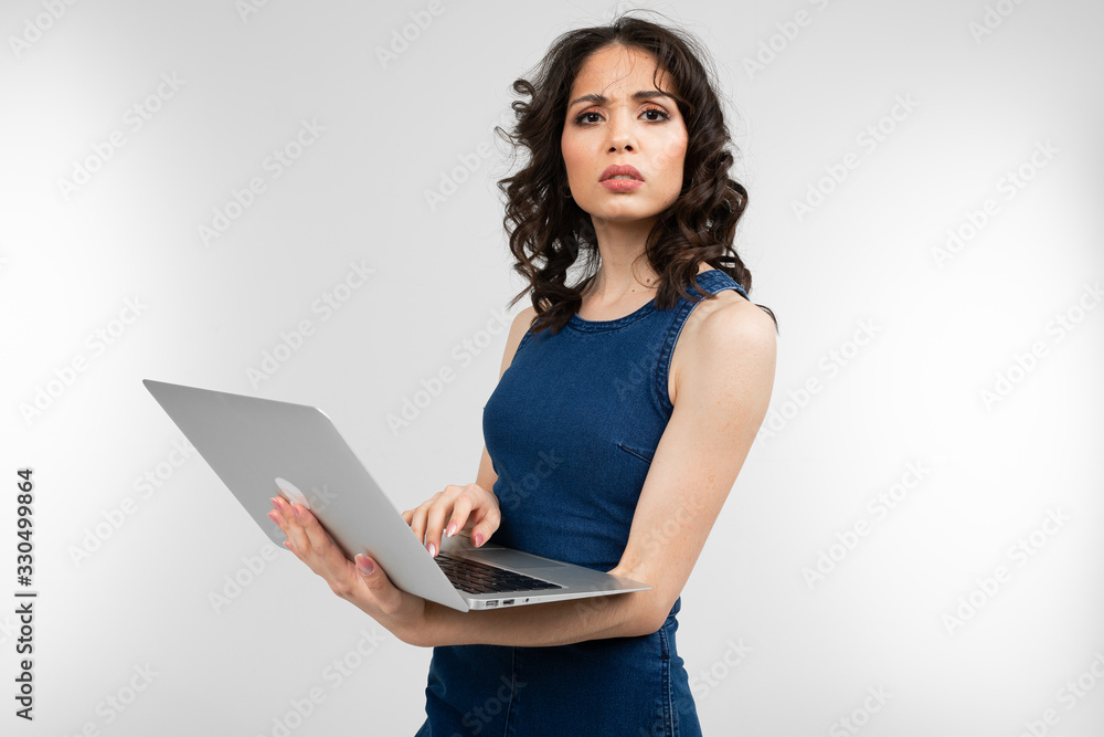 close-up of a brunette girl in a blue dress holding a laptop in her hands on a white studio background close-up of a brunette girl in a blue dress holding a laptop in her hands on a white studio background